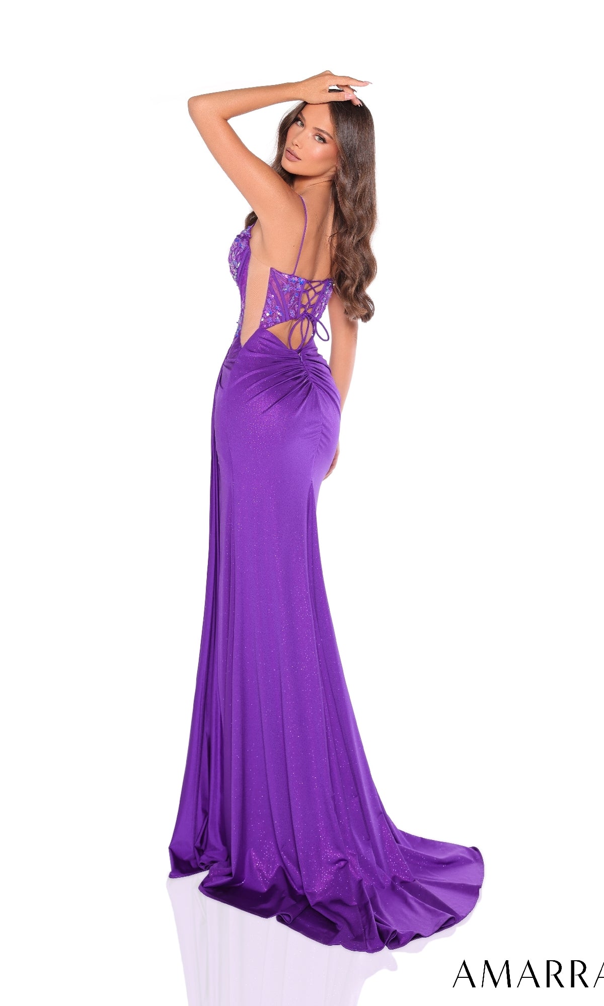 A woman poses with one arm raised, looking over her shoulder in the Amarra 88211 long purple prom dress featuring a floor-length design, backless cut, lace-up detailing, and a corset bodice.